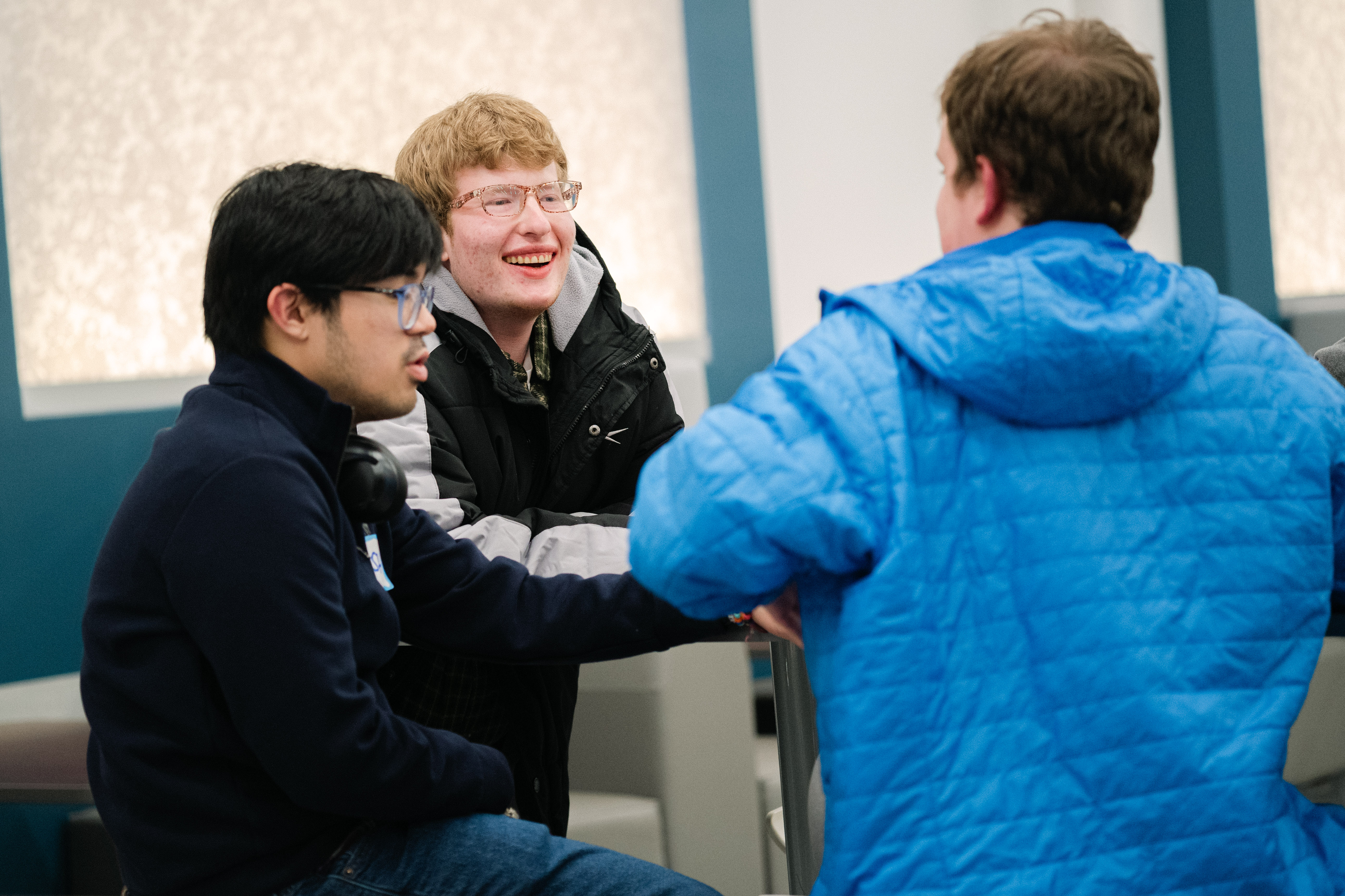Three young adult students sitting at a table and engaging in pleasant conversation.